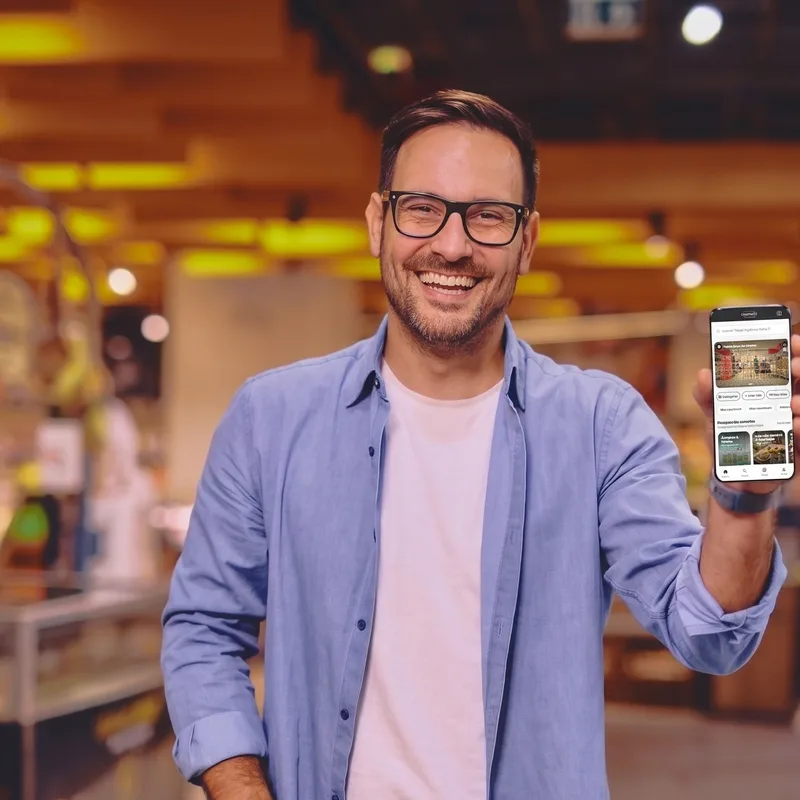 Homem sorrindo mostrando o app eopreço no celular dentro de um mercado